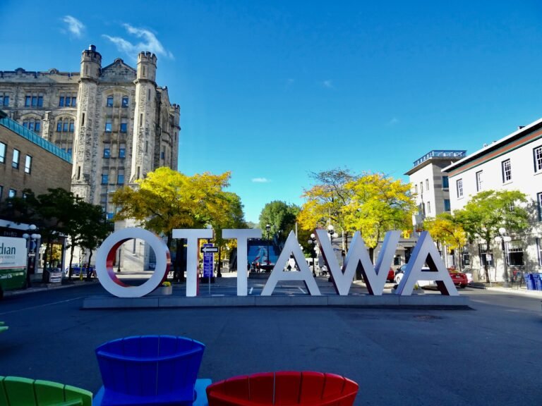 The large white and red Ottawa sign in the ByWard Market on a sunny day with historic stone buildings in the background.
