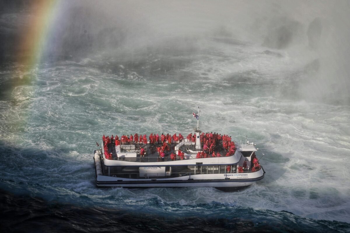 Tourists in red ponchos on a Niagara Falls cruise boat with a rainbow in the mist.